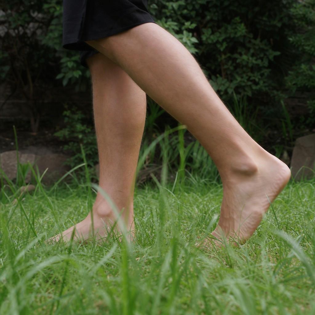 Bare feet mid-stride on grass, seen from a low side angle