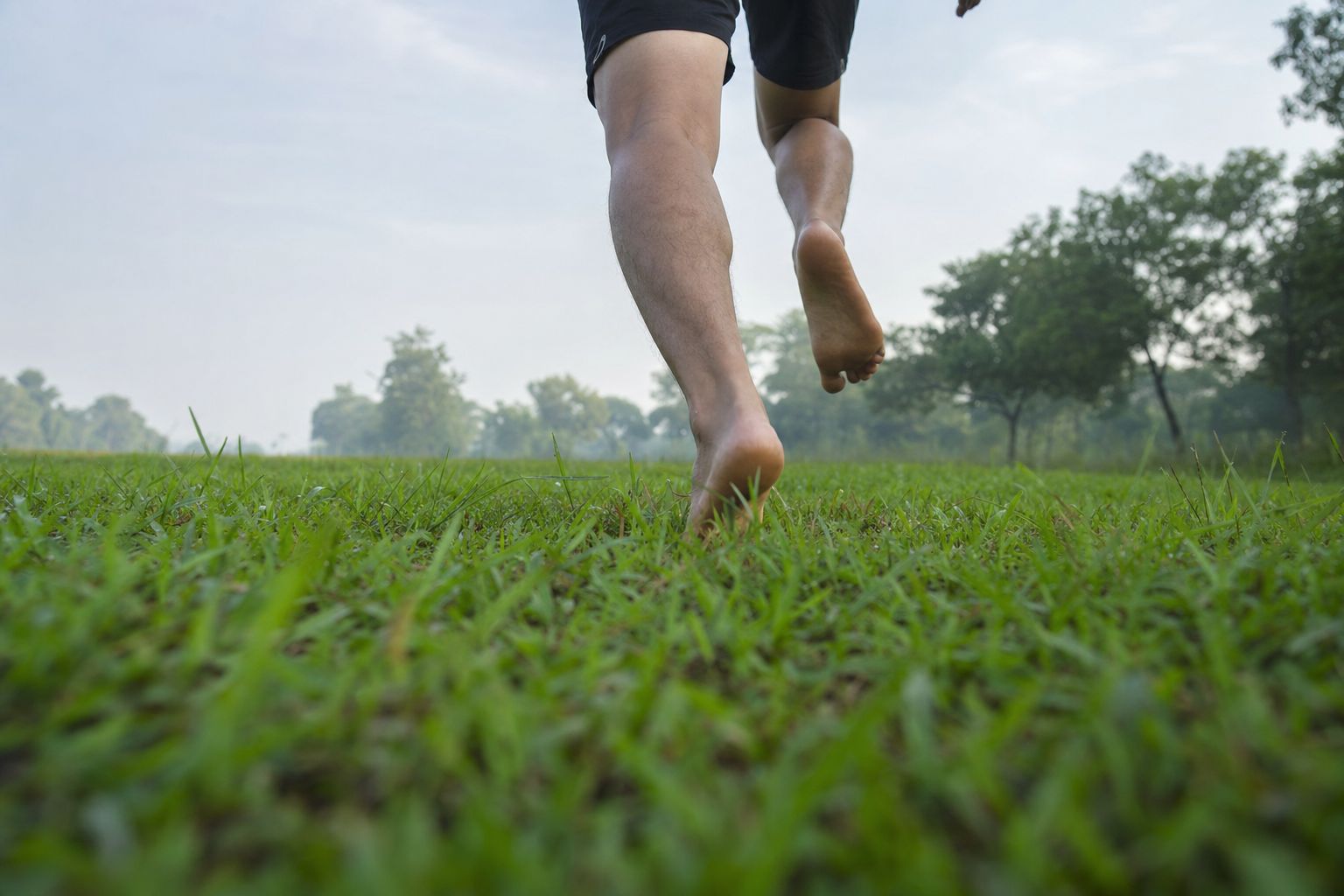 Low near-ground view of legs running barefoot on grass, knee down