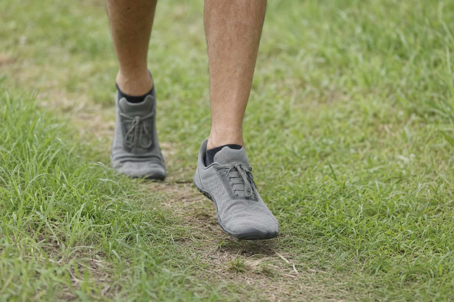 Close view of a runner's feet in minimalist running shoes on a grassy path, thin sole and wide toe box visible