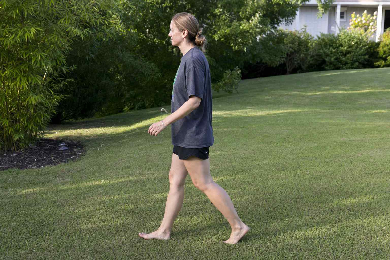 A person walking barefoot at an easy pace across a green backyard lawn
