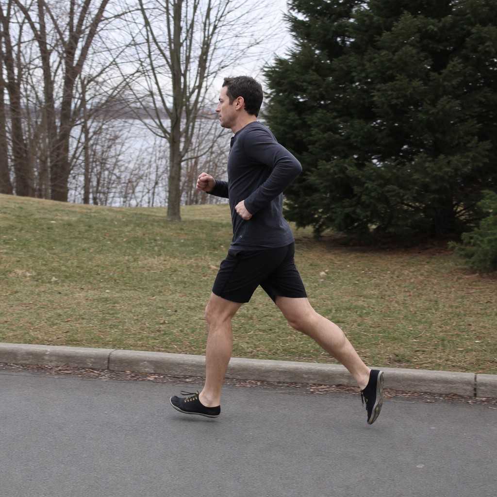 A runner in minimalist shoes on a paved path, seen from the side