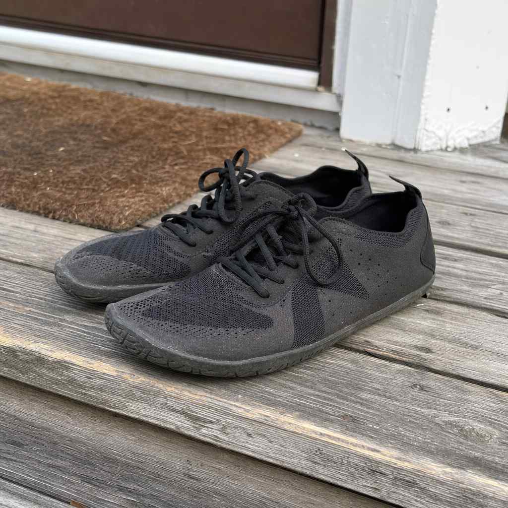 A pair of plain thin minimalist running shoes resting on a weathered wooden step