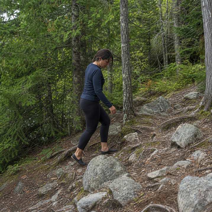 A runner stepping carefully over a rooty rocky section of trail in minimalist shoes