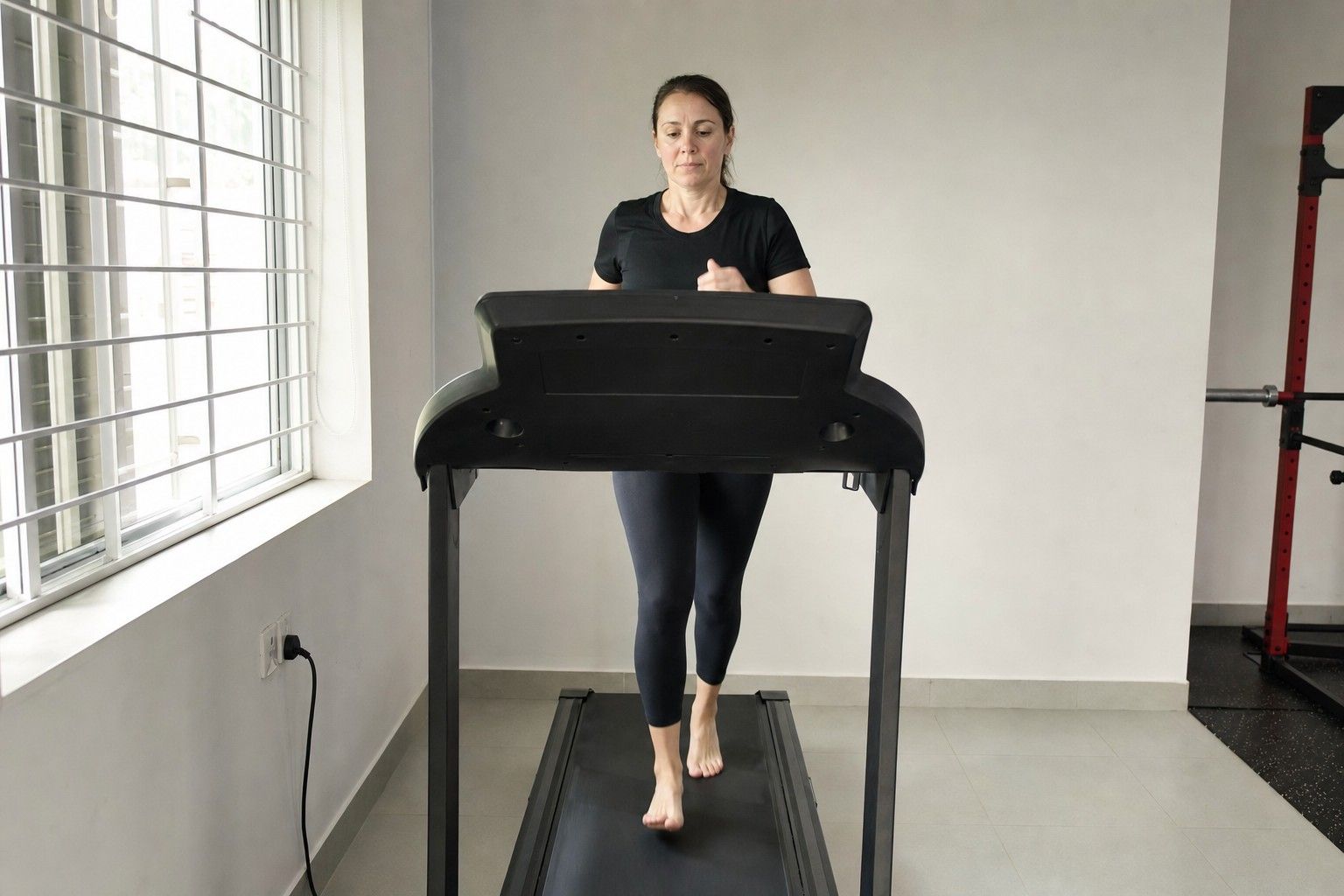 A person jogging barefoot on a treadmill indoors, seen from the front