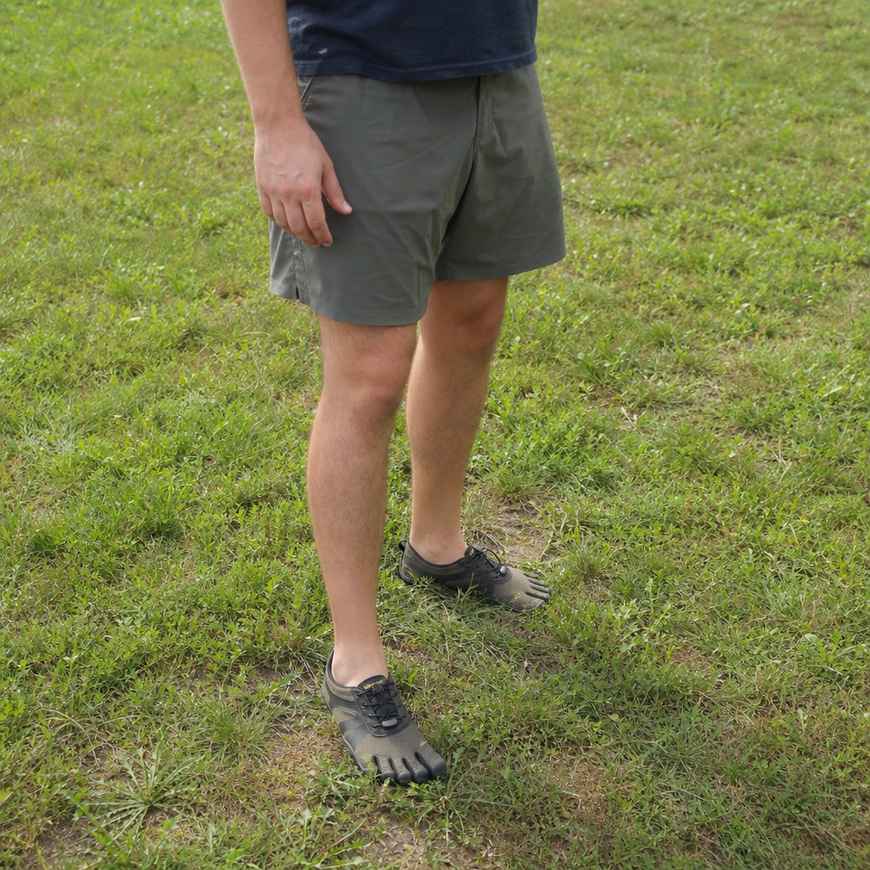 A person standing on grass wearing minimalist toe-style shoes, three-quarter mid-distance view