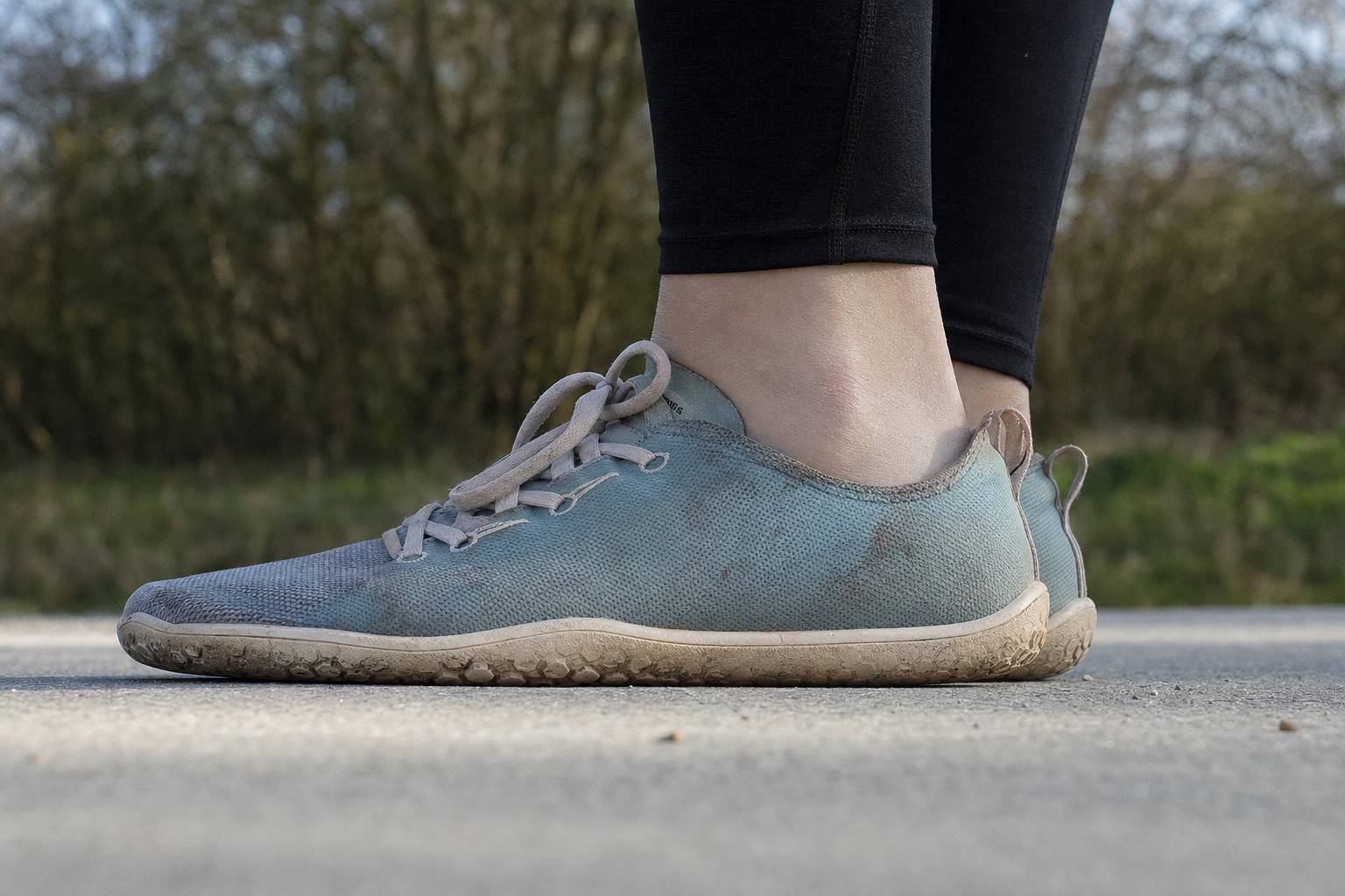 Close low side view of flat zero-drop minimalist shoes on a person's feet on pavement